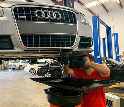 Silver Audi A4 on lift with mechanic draining coolant in preparation for removing the transmission